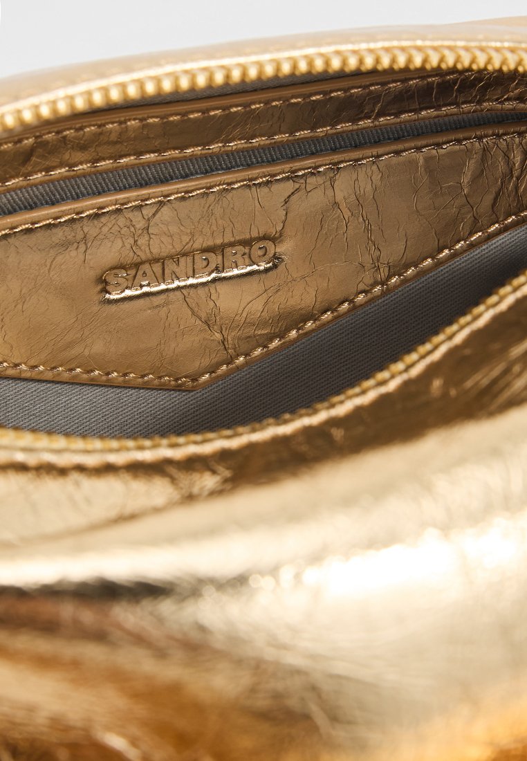 Gouden metalen pouch met een gekreukte textuur, voorzien van een grijze binnenvoering. Het merk "SANDRO" is erin gedrukt. Ritsafsluiting aan de bovenkant.