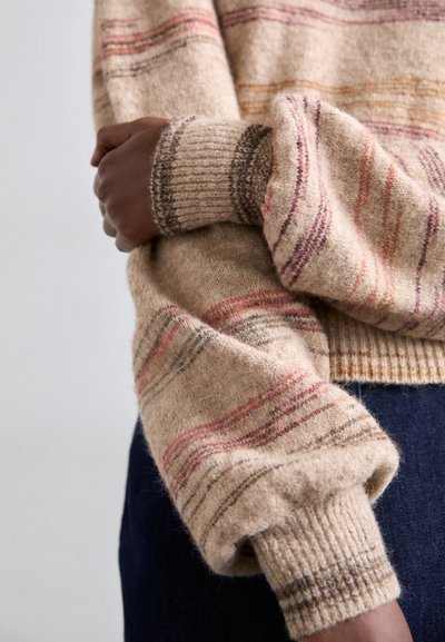 Strikkegenser i beige med flerfargede striper. Har ribbestrikkede mansjetter og en myk tekstur, med overdimensjonerte ermer og en avslappet passform.