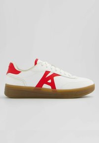 Vit sneaker med en röd "A" design på sidan, strukturerad greppsula och runda snören. Mjuk lädermaterial med slät yta.