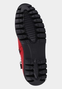 Röd sko med en strukturerad, svart gummisula som har djupa spår för bättre grepp och en slät, något böjd häl.