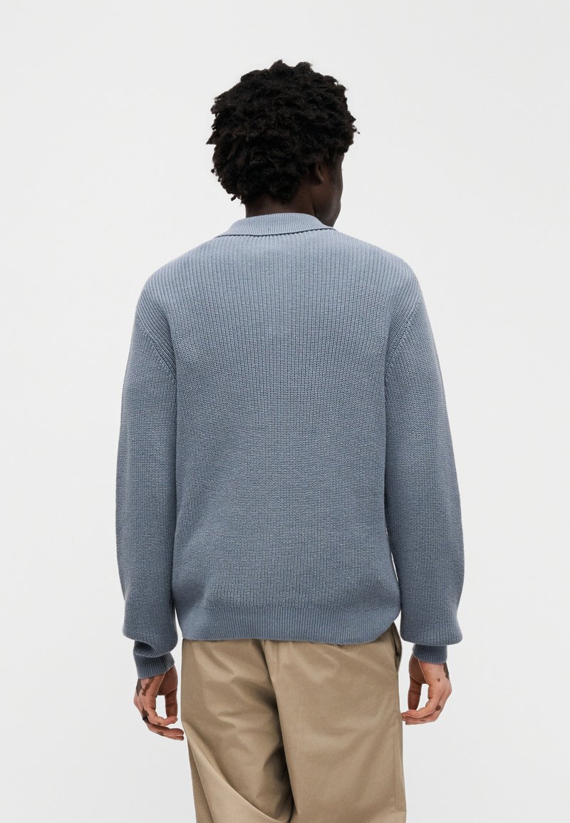 Lyseblå strikket sweater med tekstureret mønster, med rund hals og lange ærmer, kombineret med beige bukser.