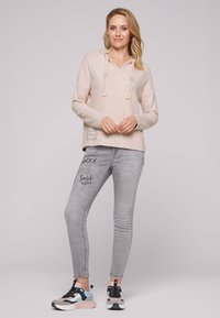 Felpa con cappuccio morbida di colore rosa chiaro, con cordini decorativi. Jeans skinny grigi con dettagli stampati. Scarpe sportive con dettagli multicolori.