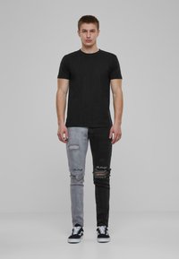 Camiseta negra de manga corta combinada con jeans bicolor: lado izquierdo gris, lado derecho negro, con detalles desgastados y texto bordado.