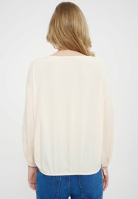 Crème-kleurige blouse met een losse pasvorm, lange mouwen, elastische onderrand en kantdetails op de mouwen, gecombineerd met high-waisted denim jeans.