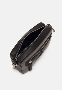 Svart lær rektangulær veske med to glidelåsrom, teksturert overflate, sølvfarget hardware, og en frontlomme med glidelås.