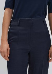 Pantalons ajustés bleu marine avec une texture lisse, dotés d'un pli avant et de poches latérales discrètes, associés à un haut bleu marine uni.