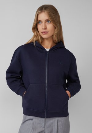 Navy zip-up hoodie made of cotton blend fabric. Features a front pocket, ribbed cuffs, and subtle logo detail on the chest.