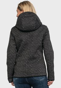 Dunkelgrau gemusterte Jacke mit Kapuze, strukturiertem Stoff und einfarbigem schwarzem Saum sowie Bündchen. Getragen mit blauen Jeans.