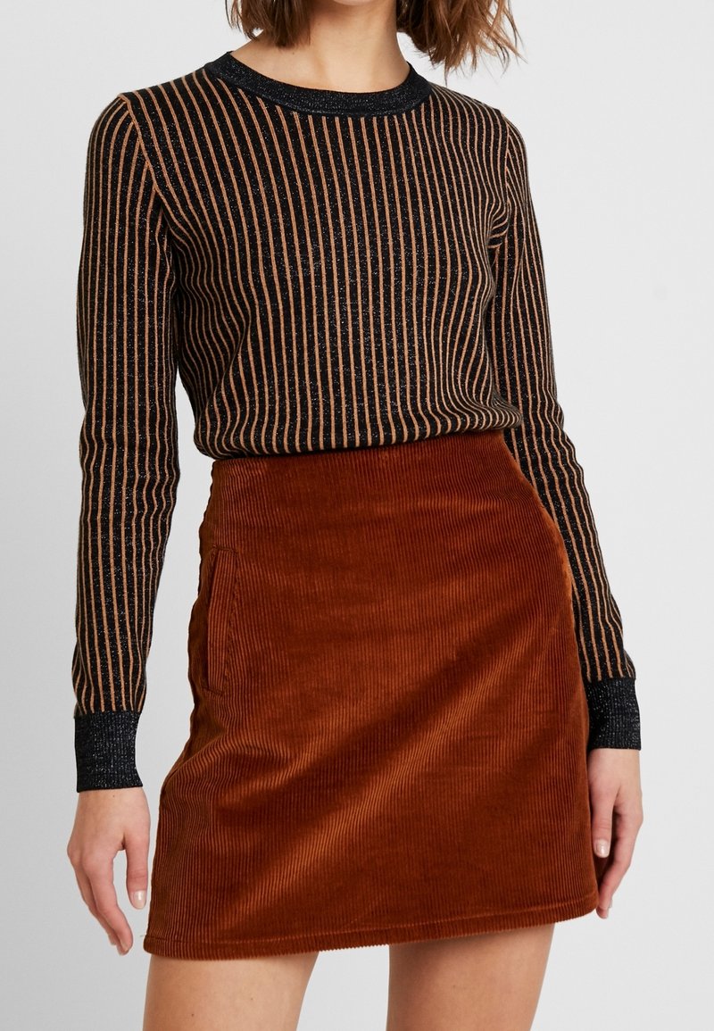 Haut à manches longues rayé noir et cuivre avec des détails scintillants, associé à une jupe en velours côtelé rouille texturée avec poches latérales.