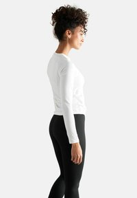 Hvid langærmet top lavet af glat stof, parret med sorte tætsiddende leggings. Sættet har et enkelt design og ingen synlige mønstre.
