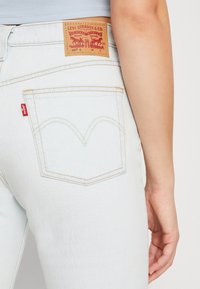Los jeans de mezclilla azul claro cuentan con una etiqueta de cuero con el logotipo de la marca, costuras amarillas y un diseño distintivo en el bolsillo trasero con un patrón arqueado.
