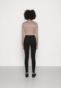 Långärmad beige topp och svarta leggings. Leggings har en hög midja och ett mjukt, elastiskt tyg. Toppen har en figurnära design.