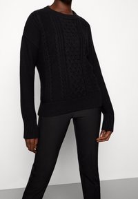 Mustat neulotut neuleet, joissa on tekstuuriin perustuva kaapelikuvio, ribbaustakit ja helma. Yhdistetty tiukkoihin mustiin housuihin.