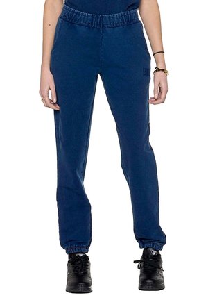 Modèle portant un pantalon de jogging bleu marine à taille élastique haute et aux chevilles resserrées, associé à des baskets noires.