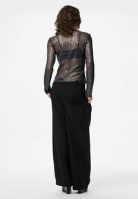 Svarta vida byxor i kombination med en åtsittande, genomskinlig topp med silverpaljetter och långa ärmar. Baksidan har en meshdesign.