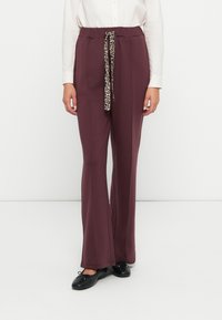 Pantalons larges bordeaux avec une taille élastique et un détail de nœud en imprimé léopard. Le tissu a une texture lisse avec des poches latérales.