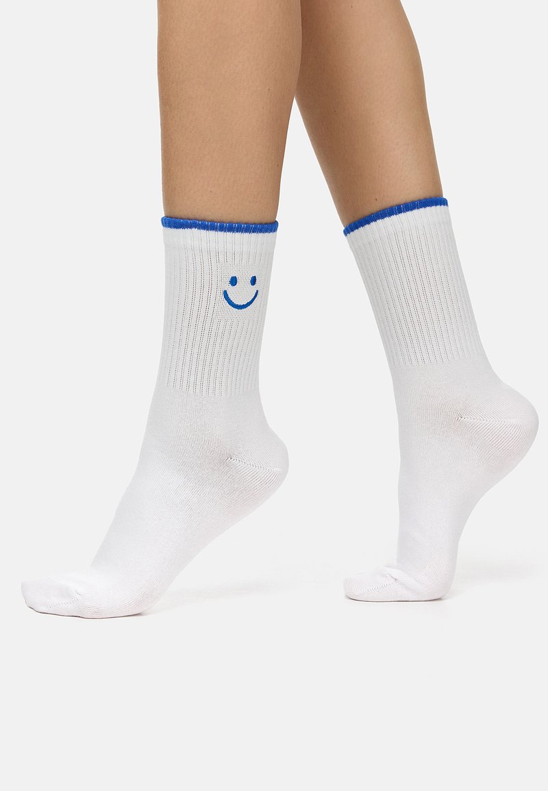 Hvide bomuldsokker med lodret ribbede detaljer, blå kant foroven og et blåt smilende ansigt grafisk tryk på siden. Kort design, fodlængden synlig.