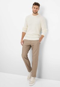 Pull en tricot crème avec texture côtelée, associé à un pantalon marron clair arborant un motif subtil. Chaussures sont des baskets beiges.