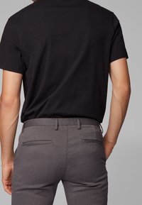 Svart bomullströja kombinerad med grå texturerade byxor med slim fit, bältesloopar och bakfickor; visad bakifrån.