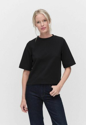 Svart kortärmad topp i bomull med rund halsringning, med avslappnad passform och minimalistisk design, kombinerad med mörka jeans.