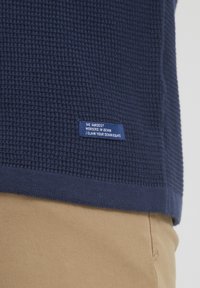 Mornarsko teksturirano pleteno pulover s rebrastim robom in modro etiketo z napisom "NAJTEŽJI DELAVCI V DENIMU / ZANESITE SVOJE DENIM PRAVICE."