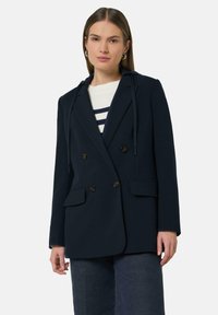 Marineblauwe dubbelgeknoopte blazer met knoopsluiting, twee voorke pockets en een capuchon. De stof heeft een gladde textuur zonder patronen.