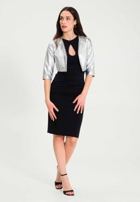 Zwarte, aansluitende jurk met een kniehoogte zoom en een keyhole halslijn, gecombineerd met een cropped, metallic zilveren jas. Zwarte enkelschoenen met een bandje.