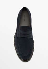 Marineblauwe suède loafers met een gestikt ontwerp en een platte rubberen zool, voorzien van een kleine decoratieve rand op het bovenwerk en een gladde textuur.