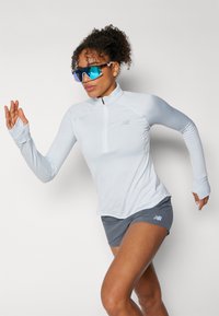 Helles blaues langärmeliges Sportshirt mit Viertelreißverschluss und Daumenlöchern, kombiniert mit grauen Shorts. Besitzt ein dezentes Streifenmuster.