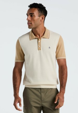 Beige en crèmekleurig polo-shirt met korte mouwen, een kraag, drie knopen en een klein logo. Zachte textuur met contrasterende mouwkleuren.