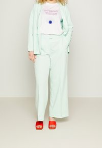 Conjunto de traje verde menta claro con pantalones de pierna ancha y una chaqueta a juego. Debajo, una camiseta blanca con texto rosa y un gráfico de un ojo azul. Sandalias de tacón bloque rojo brillante.
