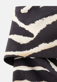 Tela de patrón en negro y beige con superficie texturizada, con rayas abstractas que parecen olas y un borde doblado.