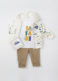 Felpa bianca con zip e stampa safari colorata, t-shirt bianca con la scritta "SAFARI" in lettere grasse, e pantaloni corti beige arrotolati. Include una scheda fotografica.
