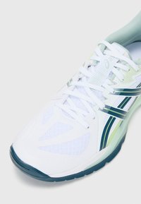 Pantof de sport alb cu un material din plasă, accente verzi și bleumarin, vârf rotunjit și șireturi. Are o talpă căptușită și elemente de design texturate.