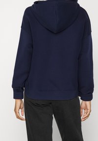 Felpa con cappuccio blu navy, dal taglio rilassato, con polsini e orlo a coste, realizzata in un morbido mix di cotone. Presenta un cappuccio ampio e spalle ribassate.