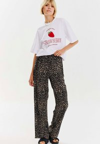 Bílé tričko s červeným potiskem "STRAWBERRY", spárované s širokými kalhotami s leopardím potiskem v černé a béžové. Hladká látka, uvolněný střih. Černé sandály.