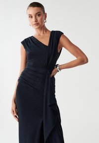 Granatowa sukienka bez rękawów z głębokim dekoltem w kształcie V, z drapowaniem, marszczonym pasem i kaskadowym detalem z materiału z połyskiem.