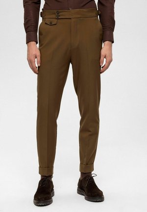 Pantalon marron sur mesure avec poches latérales, taille à deux boutons et revers pliés. Tissu lisse avec une coupe droite. Assorti à des chaussures foncées.