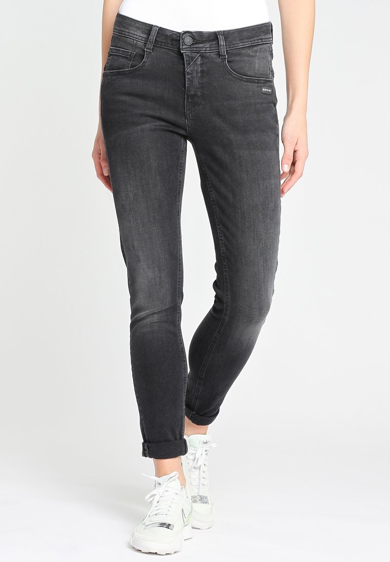 Slim-fit black denim jeans with subtle fading, five pockets, belt loops, and a cuffed hem. Styled with white sneakers.