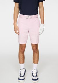 Vaaleanpunaiset golfhousut, puuvillasekoitetta, istuva malli, suora etupuoli, hopeinen vyö logolla, yhdistetty valkoisiin hansikkaisiin ja tummansinisiin lenkkitossuihin.