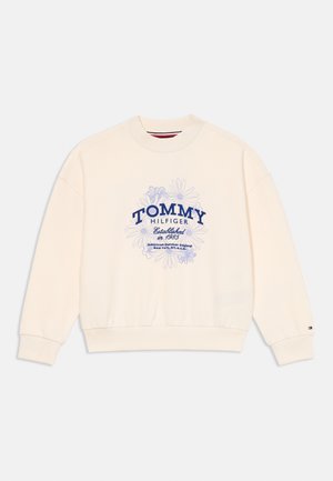 Crème oversized sweatshirt met ribgebreide cuffs en zoom. Voorkant heeft een blauwe bloemenprint en "TOMMY HILFIGER" tekst. Zachte stof, casual ontwerp.