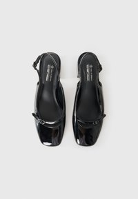 Scarpe slingback in ecopelle nera lucida con punta quadrata e tacco basso. Presentano una cinghia con una fibbia decorativa. L'interno è liscio.