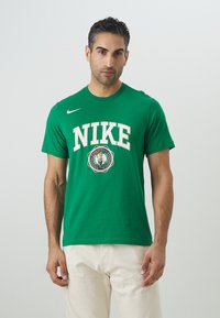 Grøn bomulds-t-shirt med hvid "NIKE" bogstaver og et cirkulært logo i midten. Slim fit, korte ærmer og rund halsudskæring.