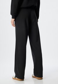 Schwarze Sweatpants aus weichem Stoff, mit einer lockeren Passform und einem elastischen Bund mit glatter Oberfläche. Dezente Seitennaht ohne Muster.