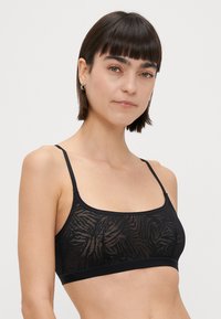 Črn modrček z prozorno vzorčasto tkanino, ki ima subtilen dizajn tigerjih črt. Prilagodljive naramnice in elastični pas na dnu.