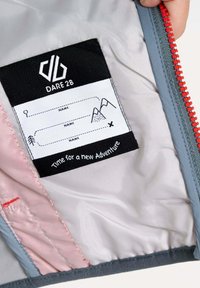 Graues und pinkes Futter der Jacke mit einem Pflegeetikett auf schwarzem Hintergrund, Platz für Namen und Berggrafiken, mit rotem Faden gestickt.