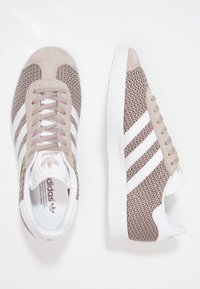 Ljusbruna och beige sneakers med en texturerad meshovandel, mockaaccenter, vita tre ränder och gummisula. Har en rund tå och snörning.