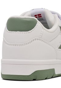 Weißer Sneaker mit einem strukturierten grünen Akzent an der Ferse, der ein glattes Lederoberteil und eine Gummisohle mit einem markanten Profilmuster aufweist.