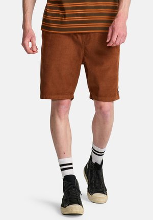Shorts di velluto a coste marroni con taglio dritto, tasche laterali e orlo risvoltato. Abbinate a sneakers alte nere e calzini a righe.