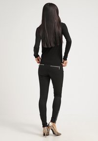 Haut noir à manches longues avec une silhouette ajustée, associé à des leggings noirs dotés de poches zippées et d'une texture lisse, porté avec des talons métallisées.